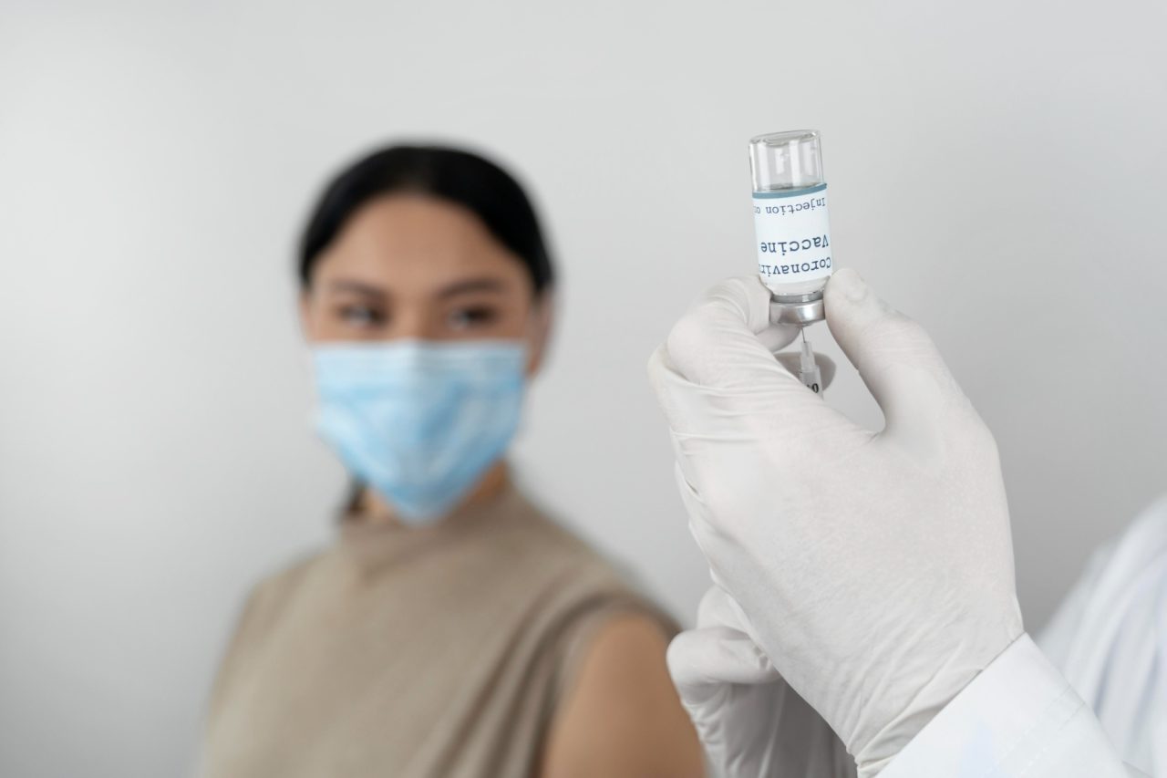 Enfermeiro com seringa pegando a vacina para aplicar em paciente que está sentada e usando máscara descartável azul