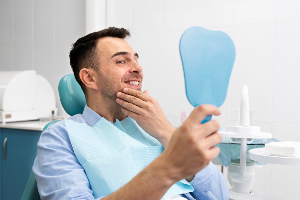 homem no dentista olhando para o espelho e sorrindo ao ver o resultado