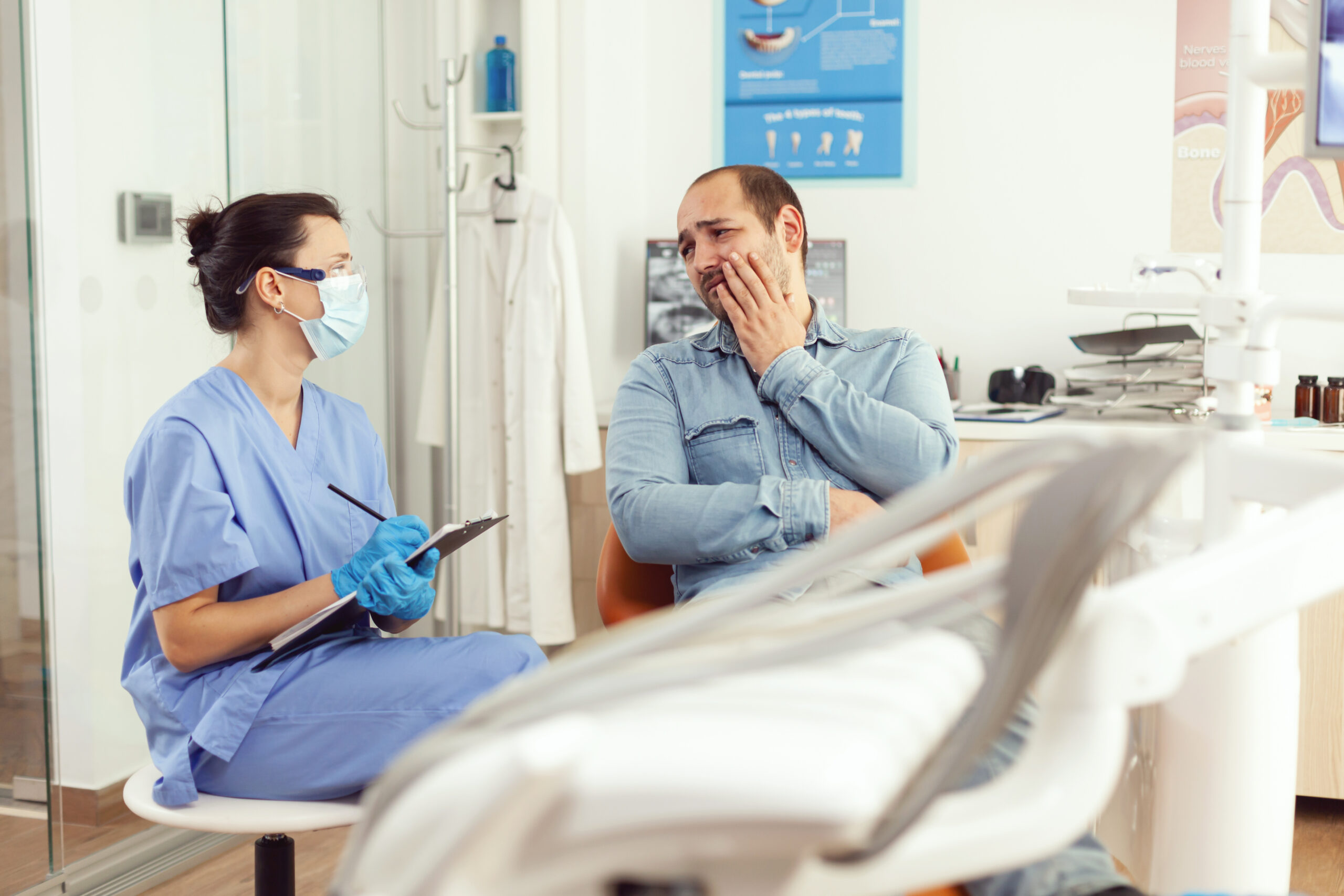 paciente com cara triste e mão em cima da bochecha explicando para dentista