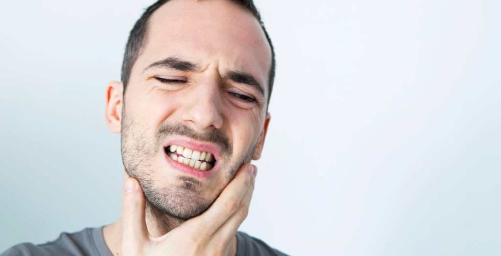 Homem apertando a mandíbula e sentindo dor. Ele apoia a mão no queixo.