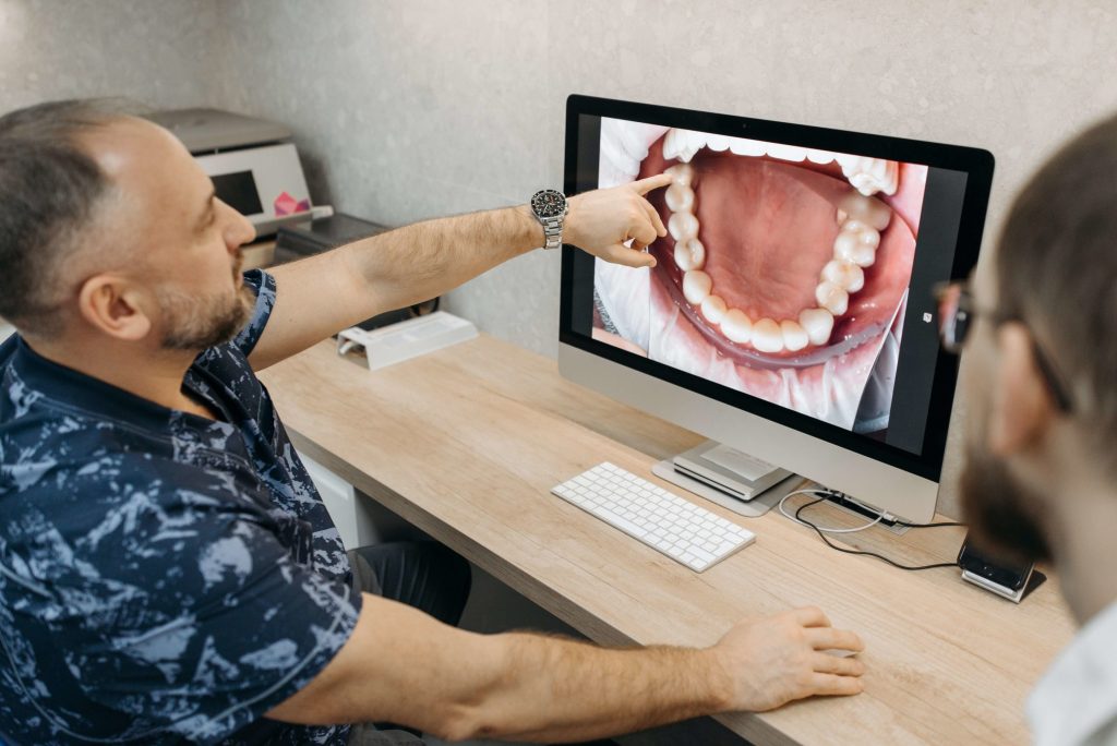 homem dentista apontando para dente na tela e mostrando para paciente - junção de fonoaudiologia e odontologia