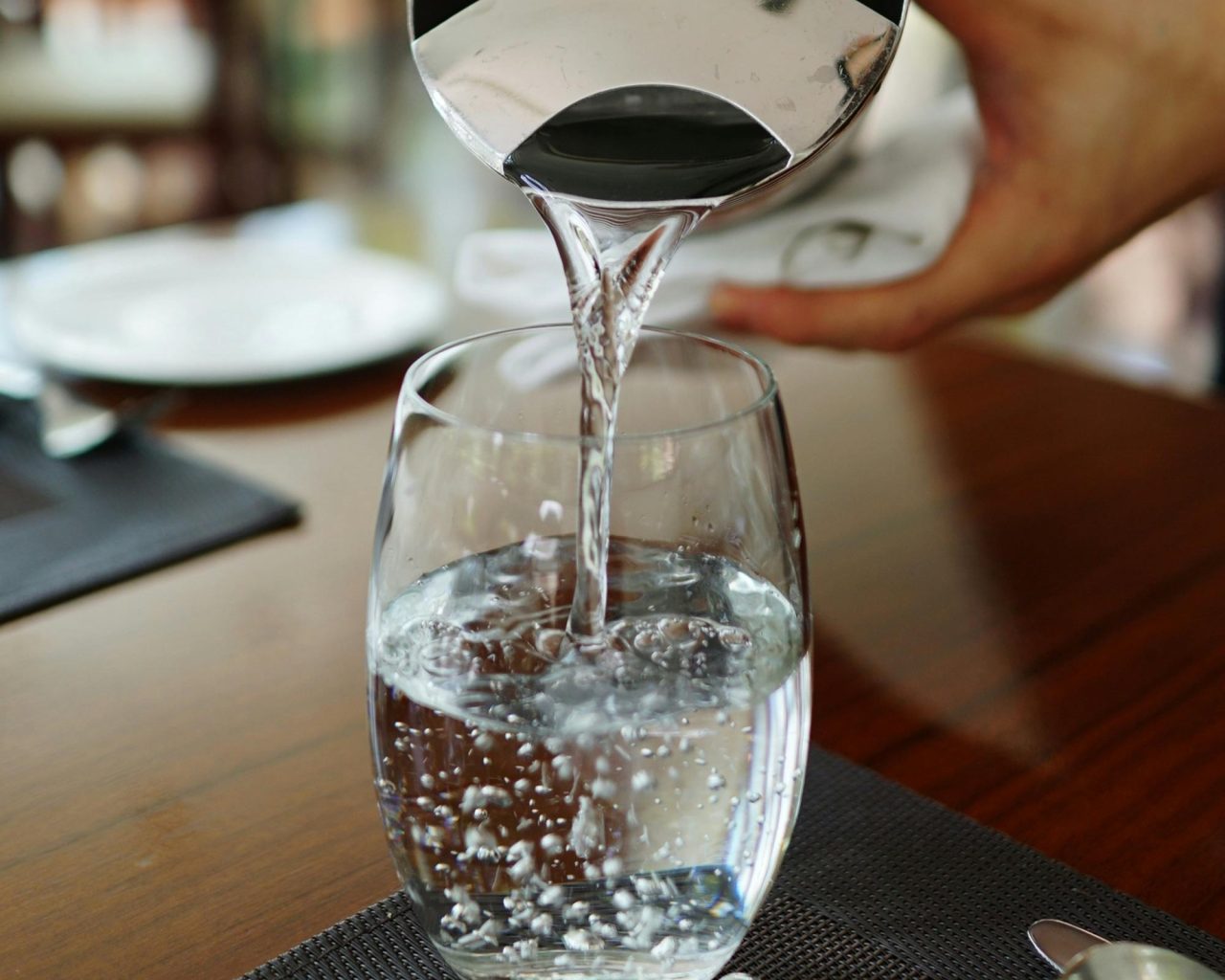 Colocando água em copo de vidro que está na mesa, com jarra.