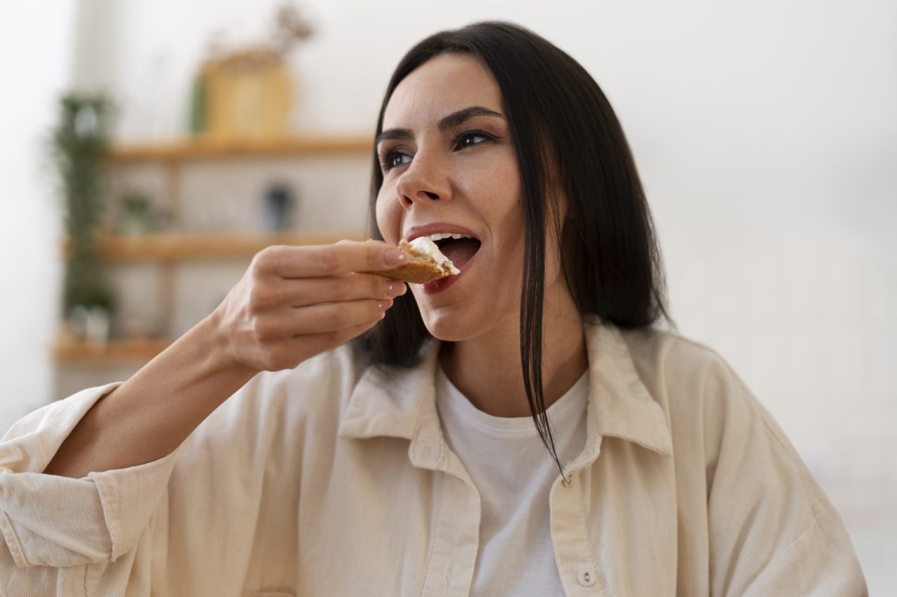 Mulher está em casa comendo com as mãos.
