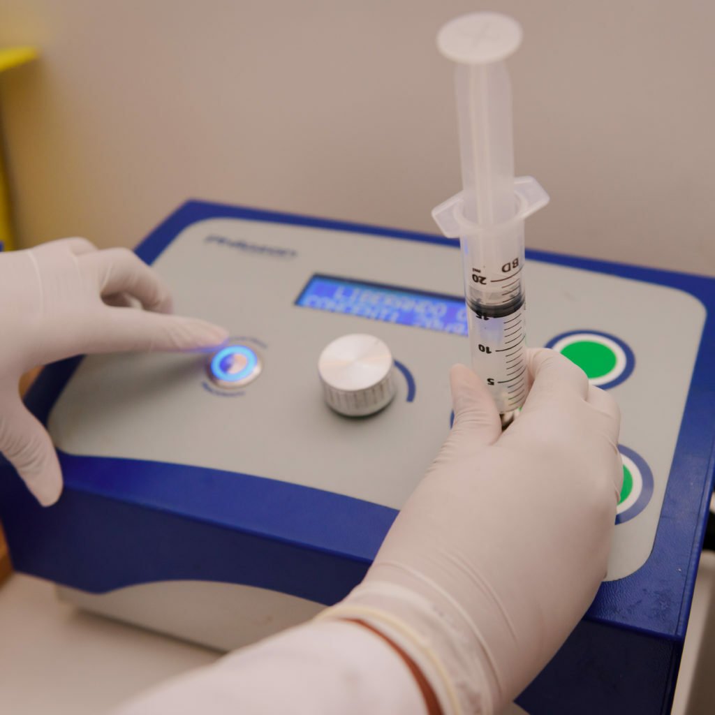 Máquina para ozonioterapia, a pessoa está usando luvas e pegando o líquido com uma seringa.