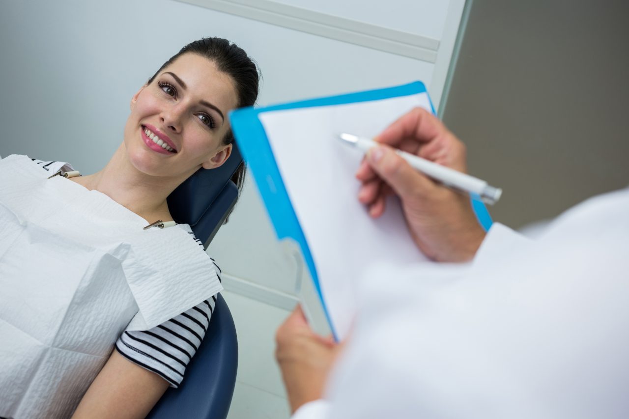 dentista anotando em um papel em branco e a paciente sorrindo esperando