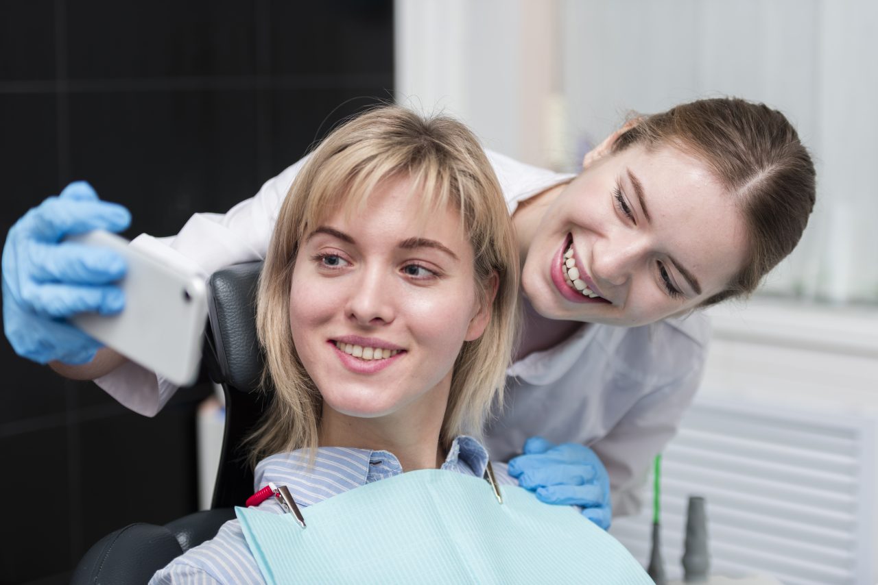 dentista mulher e paciente mulher loira tirando selfie no consultório
