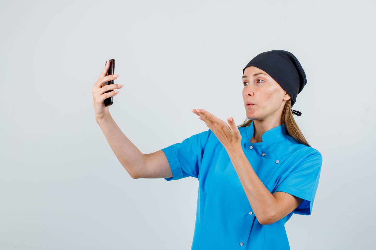 Dentista gravando vídeo pelo celular está mandando um beijo para a tela.