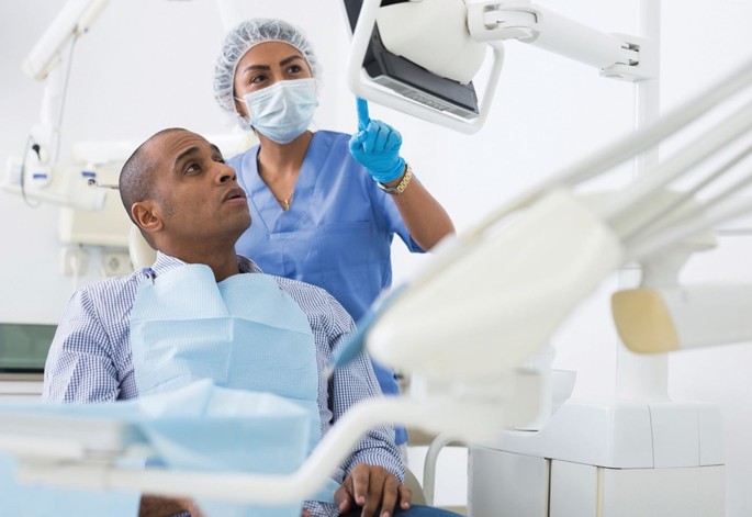 Dentista está explicando procedimento para paciente, que está sentado na cadeira odontológica olhando para a tela.
