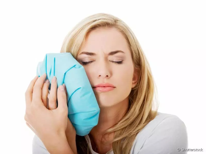 mulher loira segura bolsa de gelo em sua bochecha fazendo compressa