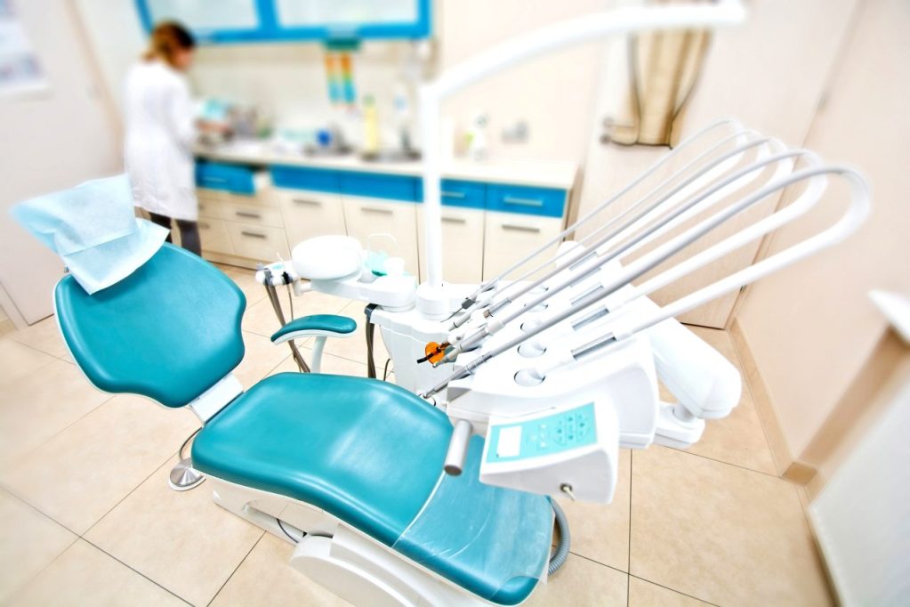 consultório de dentista, no fundo desfocado é possível ver a dentista lavando algo
