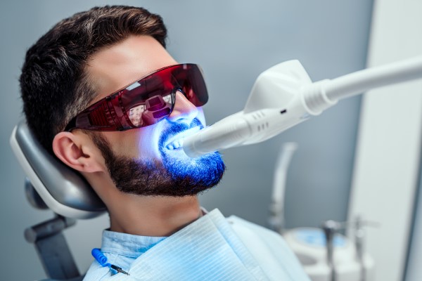 homem no dentista usando óculos de proteção, está com luz led azul nos dentes
