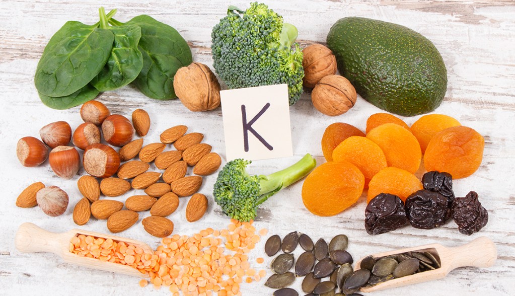 várias verduras e frutas em cima da mesa com uma placa escrito K no centro