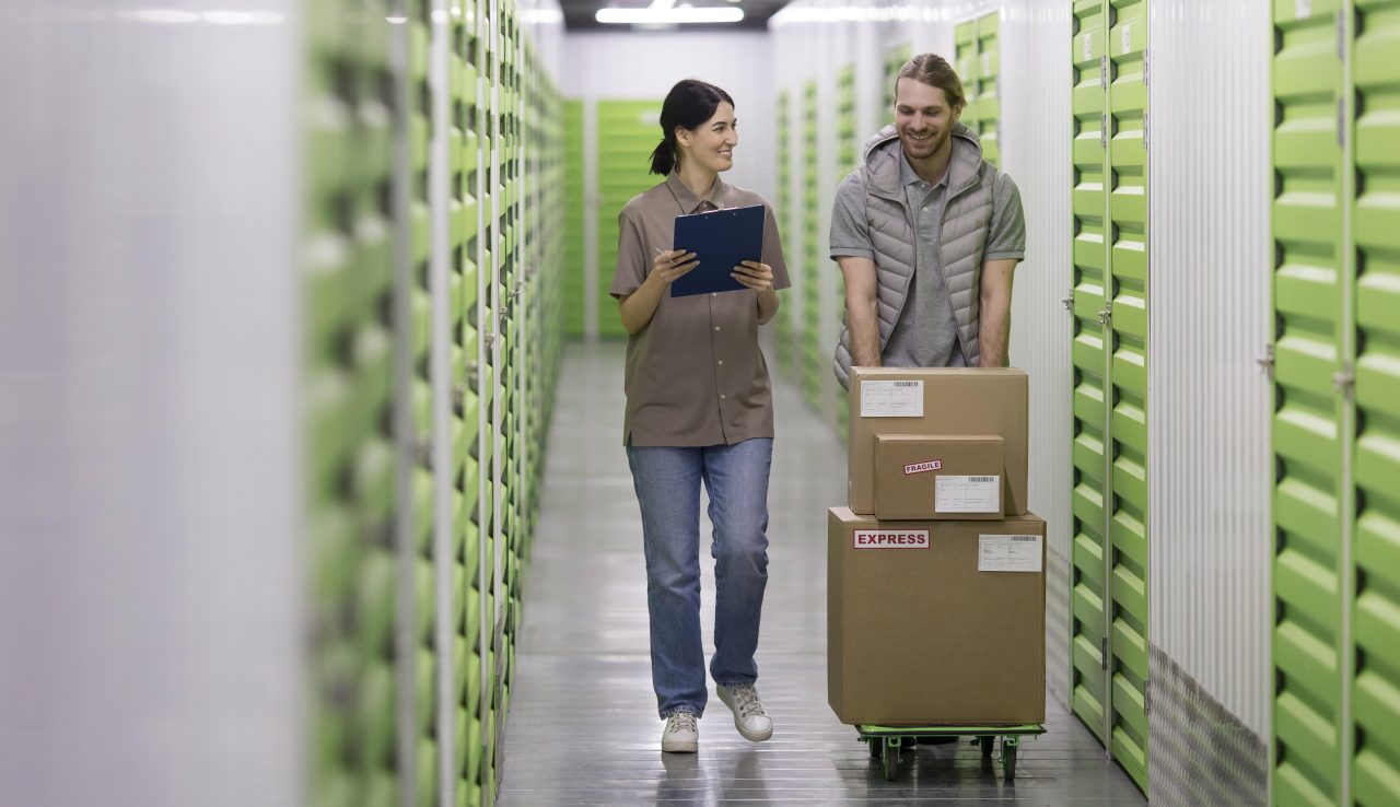 mulher andando com prancheta ao lado de homem que está andando empurrando carrinho com caixas
