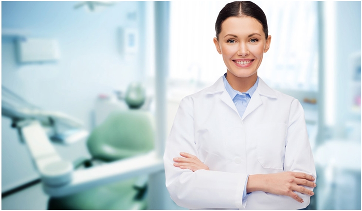 Dentista com jaleco em seu consultório de braços cruzados e sorrindo