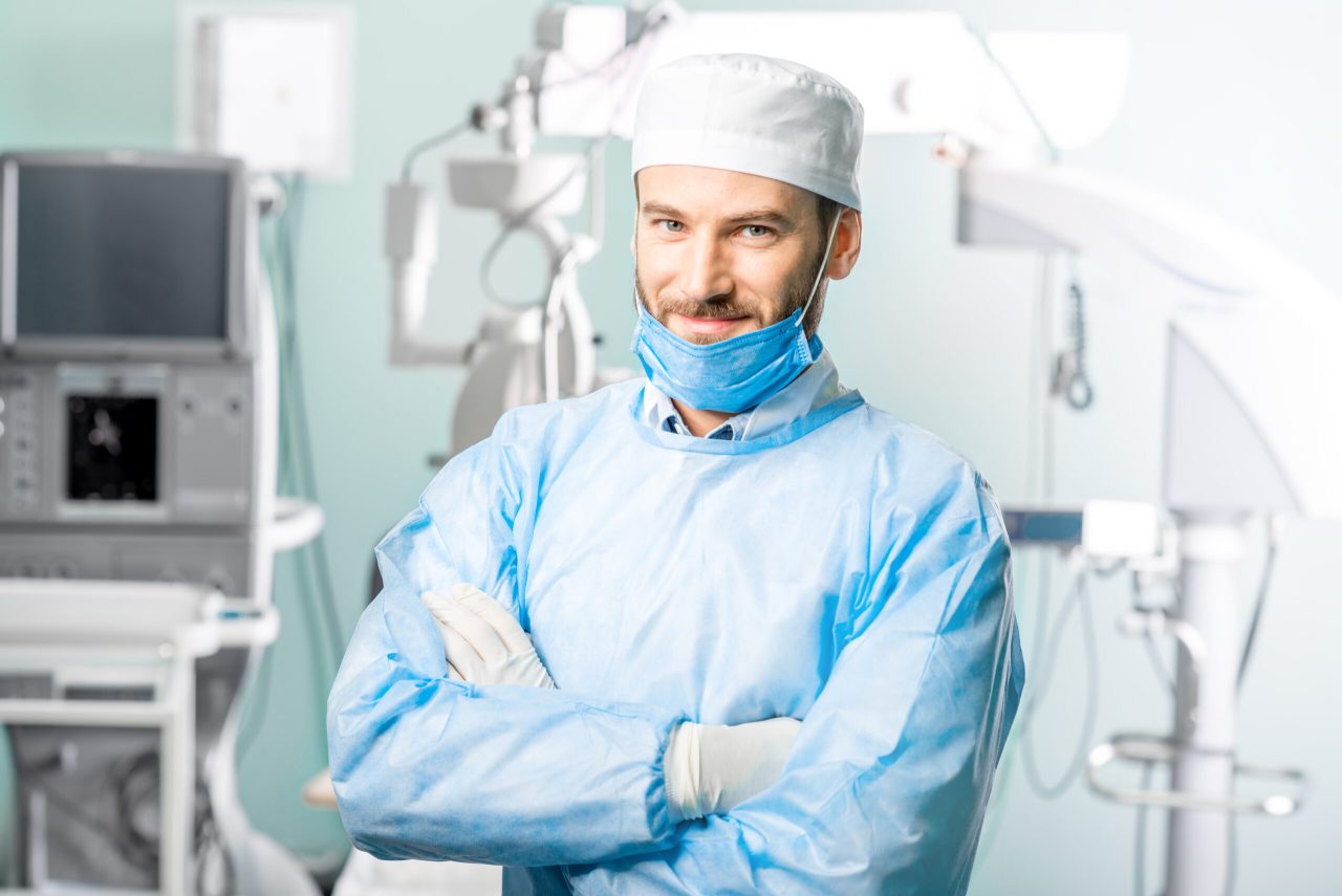 Dentista homem em seu consultório utilizando epis, ele está com os braços cruzados e posando para a foto