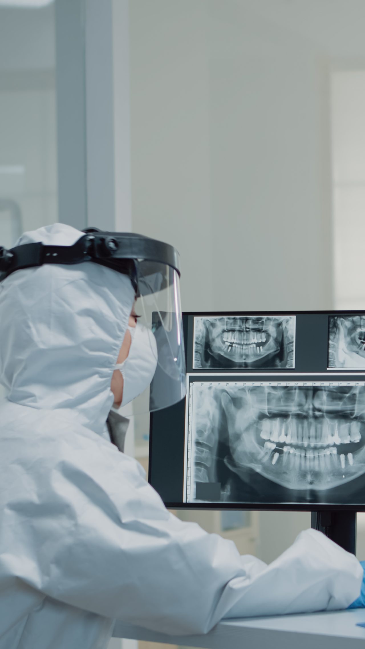 dentista com trajes epi analisando panoramas de paciente em computador