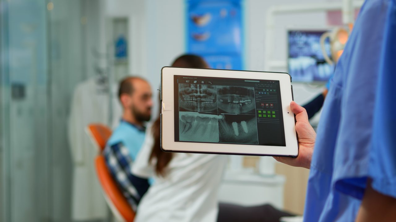 dentista em consultório segurando tablet com os raio-x na tela