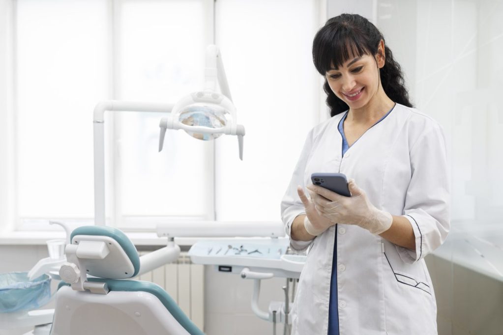 dentista em consultório sorrindo enquanto meche no celular