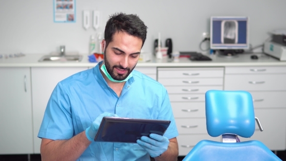 Dentista homem mexendo em tablet, sentado em seu consultório