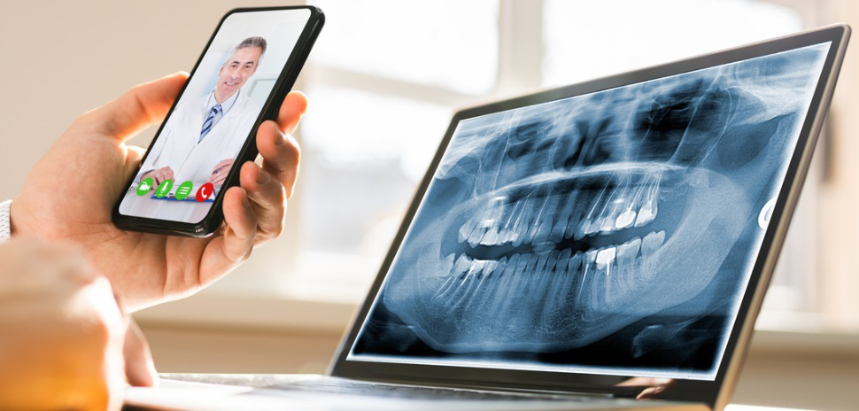 Tablet com imagem panorâmica da boca apoiado em mesa, e pessoa segurando na mão um celular fazendo videochamada com dentista