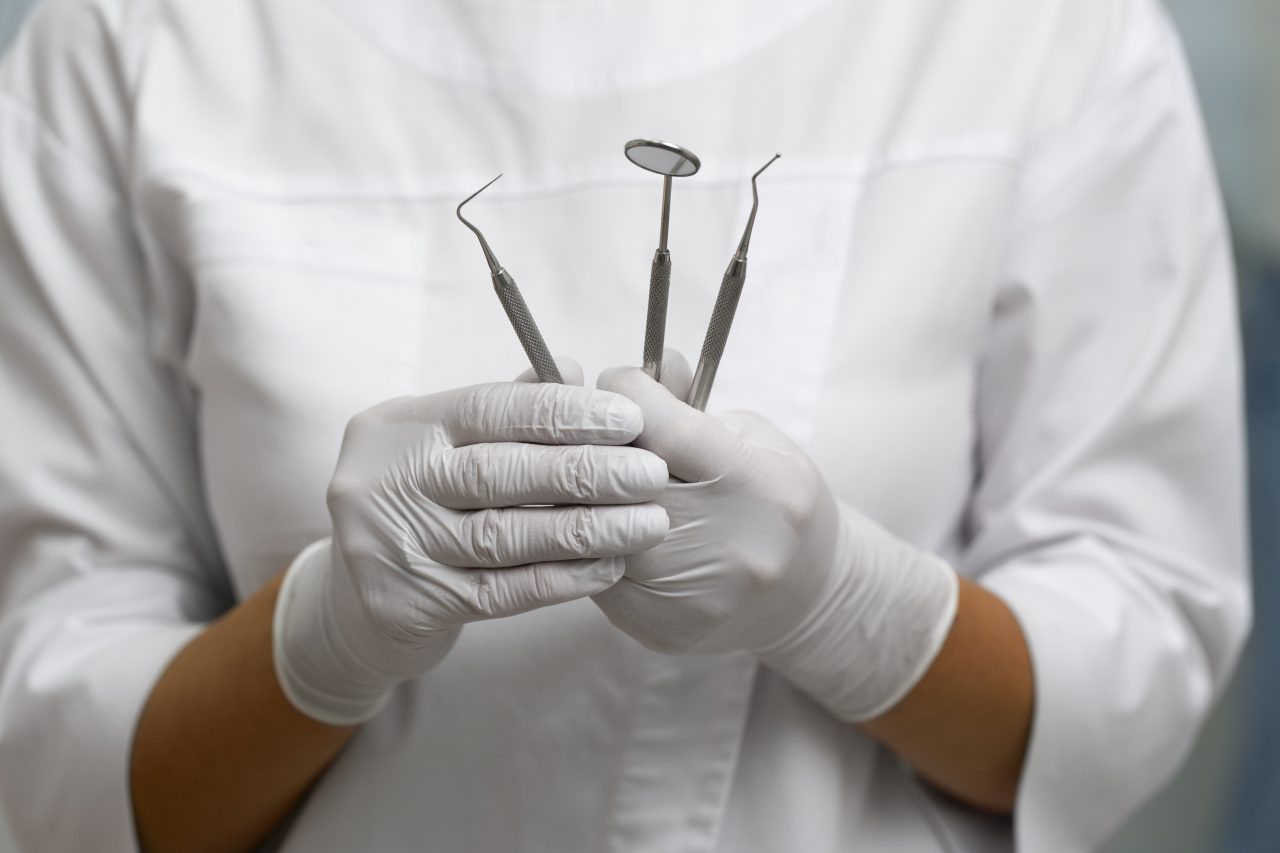 Dentista segurando alguns instrumentos odontológicos, como espelhinho