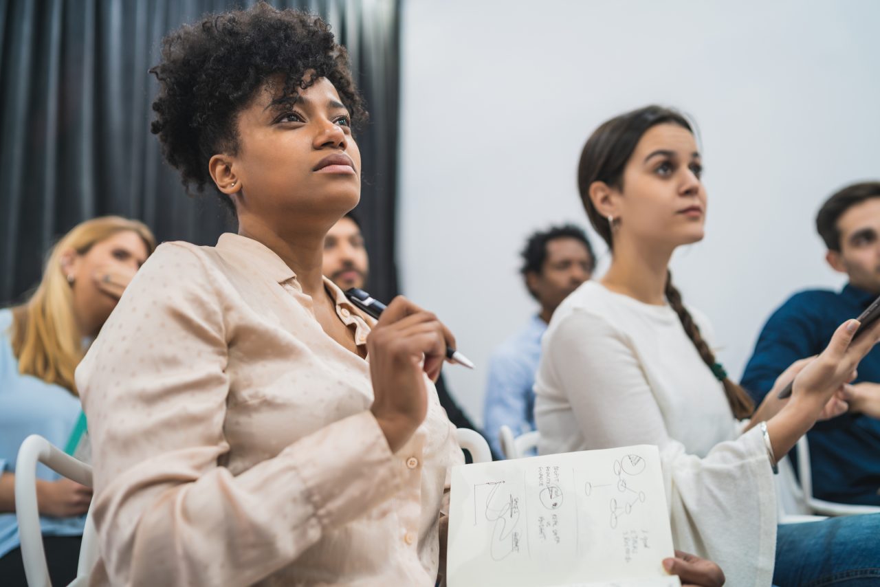 Grupo de trabalhadores em reunião fazendo um brainstom e anotando suas ideias em cadernos e celulares.