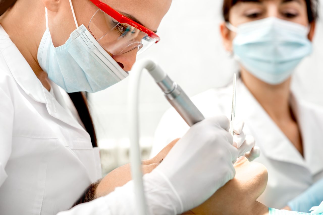 Dentista e assistente fazendo tratamento em dente de cliente em consultório odontológico
