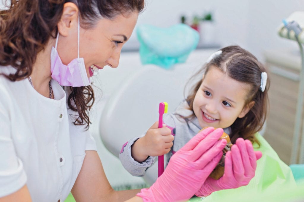 Dentista mulher com paciente criança segurando escova de dente