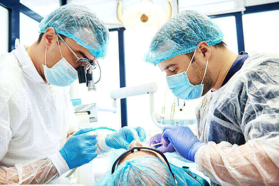 Dentistas usando EPI realizando procedimento cirúrgico em paciente