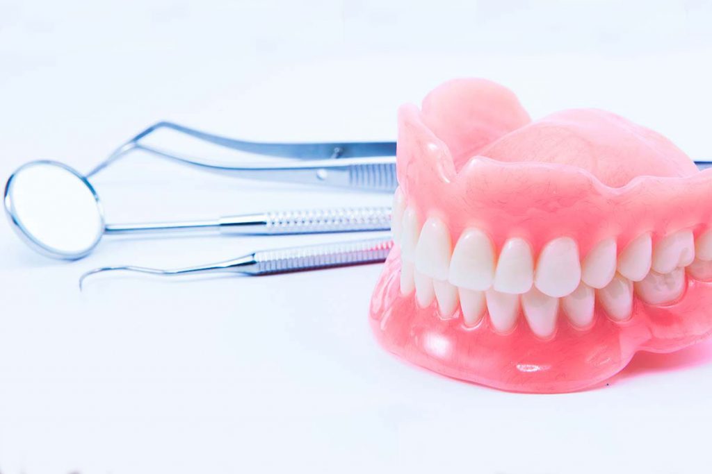 Prótese dentária e instrumentos de dentista em fundo branco - Por que fazer especialização em prótese dentária?