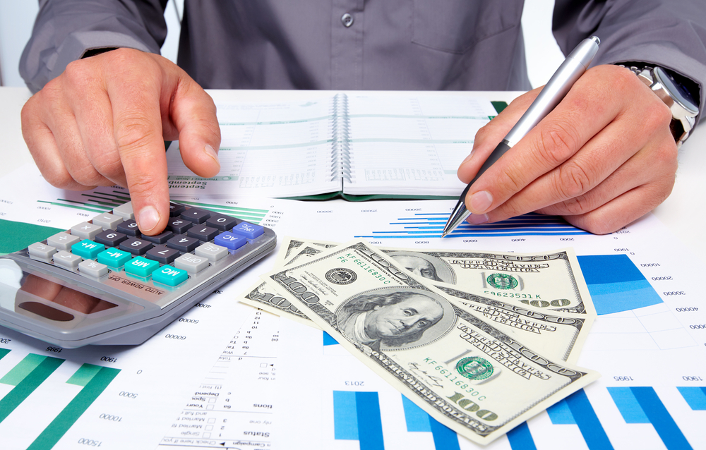Homem com calculadora, agenda, planilhas e dinheiro
