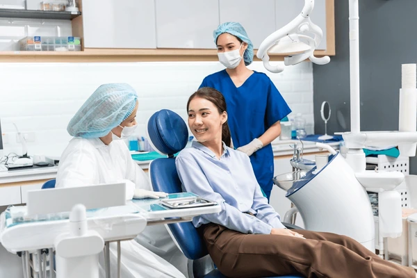 Dentista, assistente e paciente em consultório odontológico conversando felizes