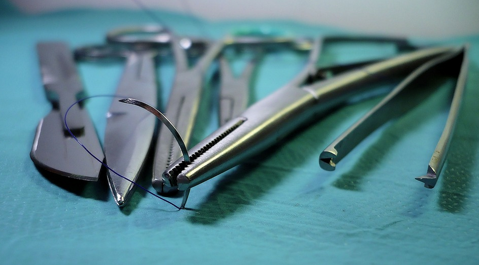 Alguns instrumentos odontológicos em cima da mesa e uma pinça segurando o fio de sutura