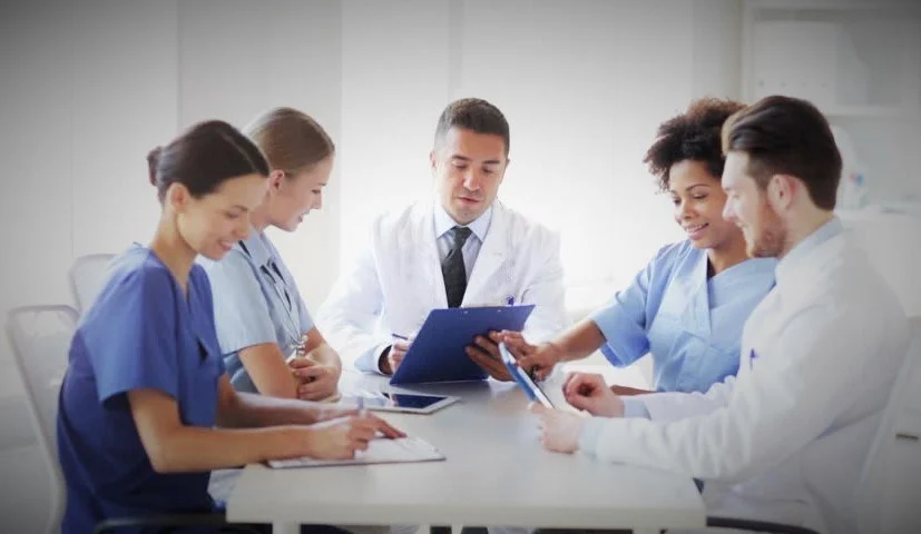 médicos e dentistas reunidos em uma mesa conversando e anotando em suas pranchetas ou tablets