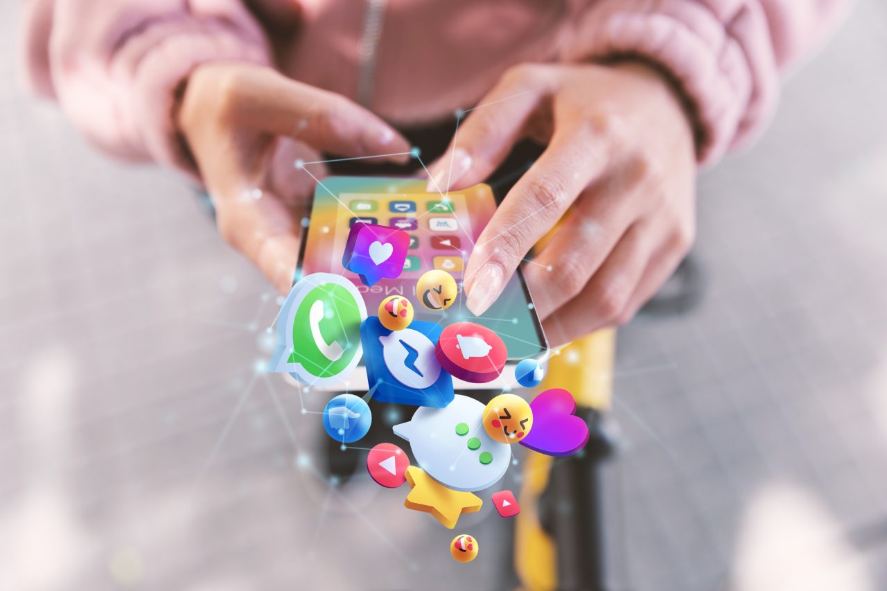 mulher segurando um celular, na tela e saindo da tela tem vários ícones de redes sociais e emojis
