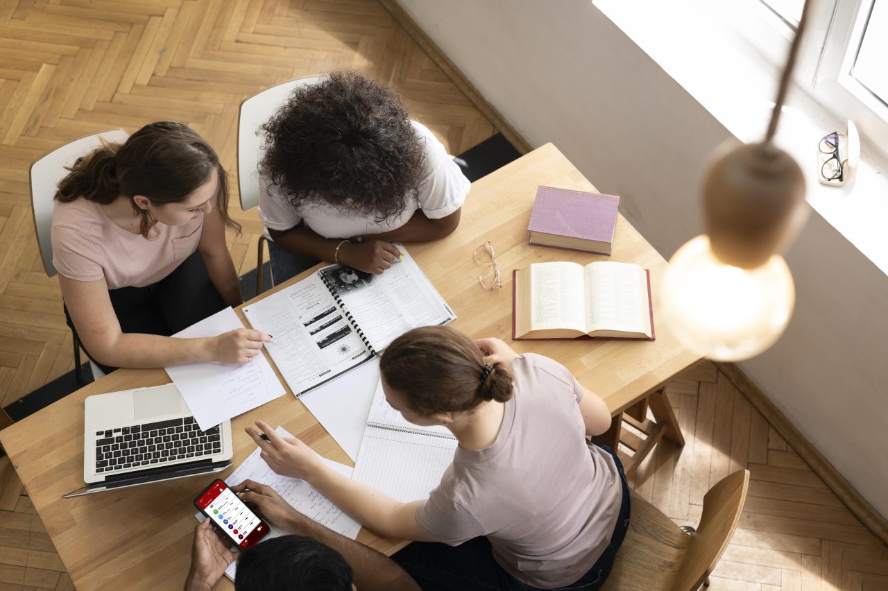 três mulheres sentadas estudandocom livros, celular e notebook