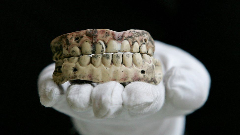 mão usando luva segurando arcada dentária completa na palma da mão