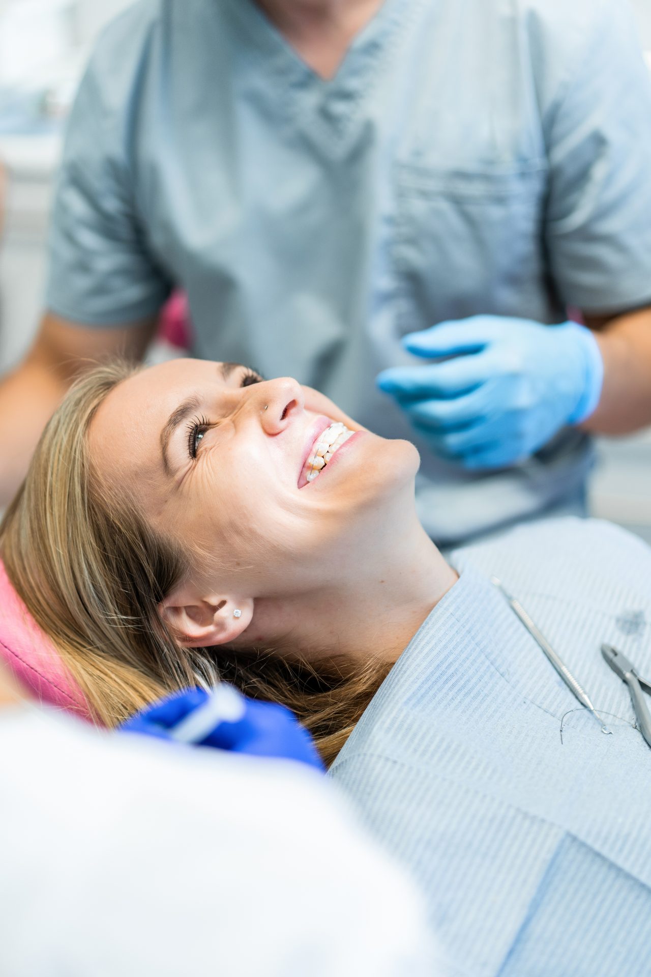 Paciente mulher loira deitada em cadeira odontológica sorrindo