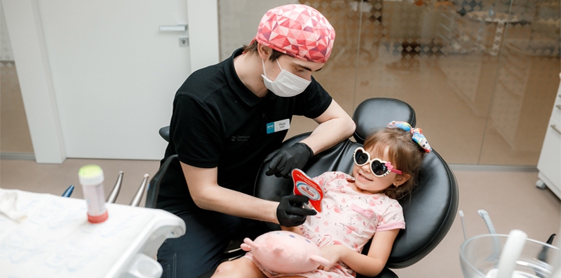 Dentista mostrando resultado de tratamento com espelho para paciente menina/criança