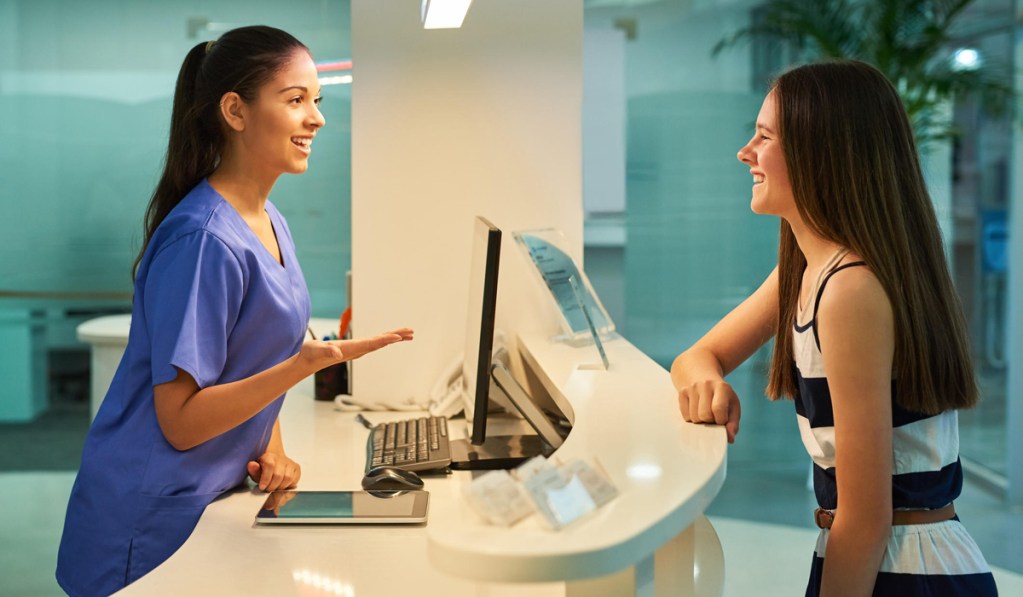 Recepcionista jovem atendendo garota que está sorrindo no balcão