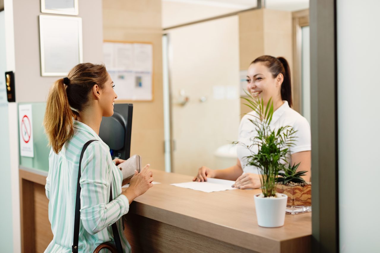 Recepcionista e paciente conversando e sorrindo em clínica