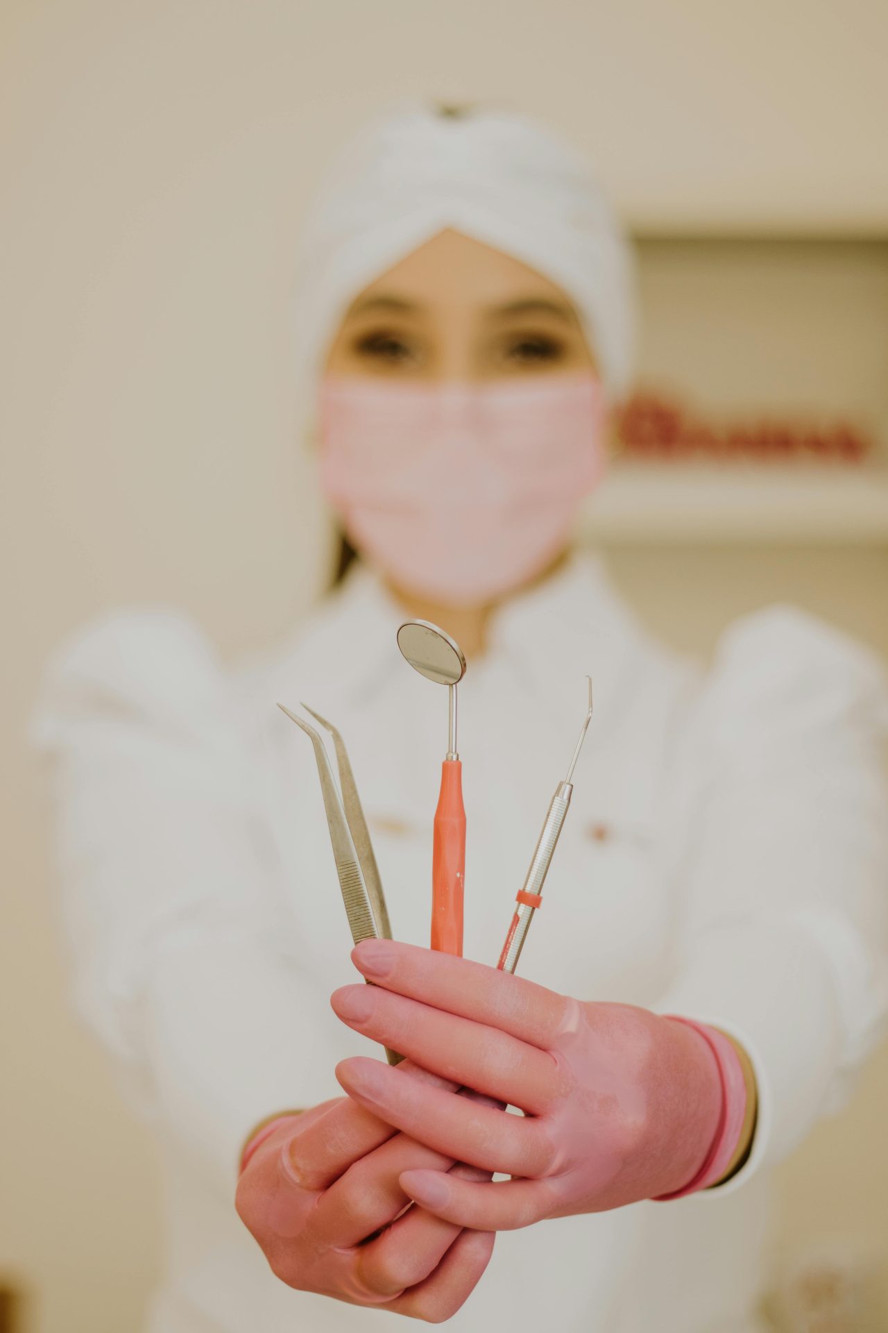 Dentista segurando alguns instrumentos odontológicos, usando luva e máscara rosa