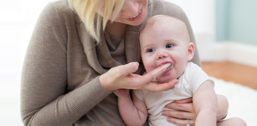 Mãe passando dedeira na gengiva das crianças