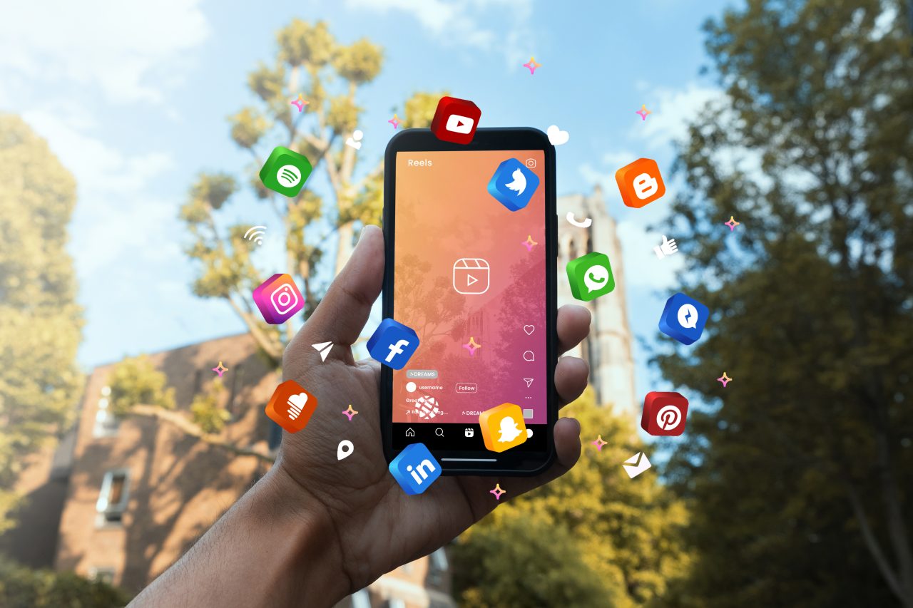 Pessoa segurando celular que está aberto em vídeo em uma rede social. Ao redor do celular tem vários ícones de redes sociais flutuando.