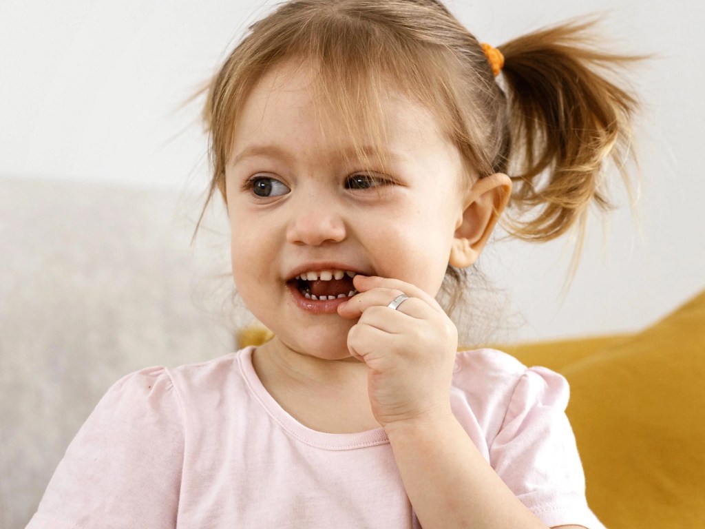 criança colocando um pequeno pedaço de chocolate na boca. Ela tem cabelo loiro que está preso em maria chiquinha.