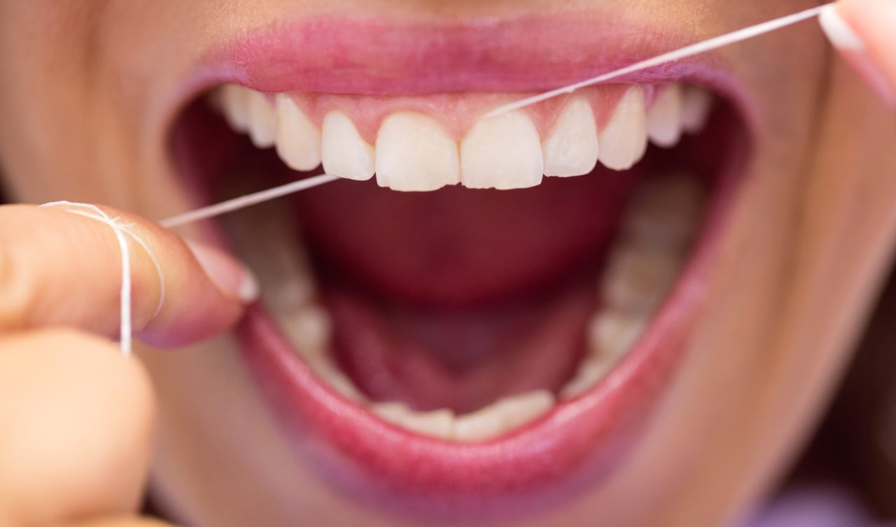 mulher passando fio dental nos dentes