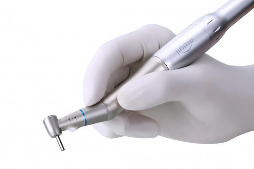 Mão com luva branca segurando broca odontológica