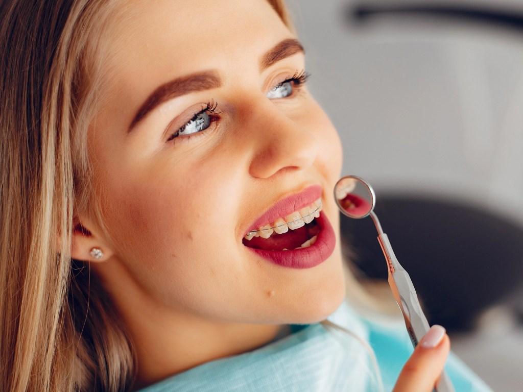 Paciente loira no dentista, está analisando seu aparelho ortodôntico