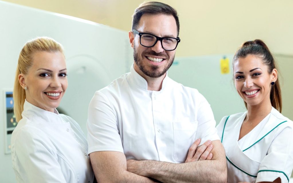 Equipe de três dentistas sorrindo em consultório.