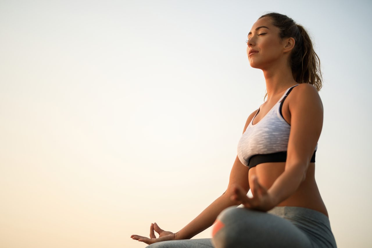 Mulher meditando, utilizando roupas de ginástica e cabelo em rabo de cavalo